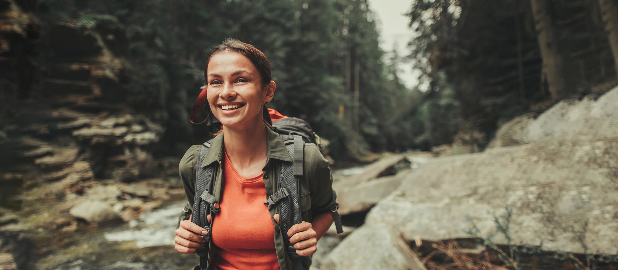 young happy female hiking through rocky water stream